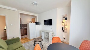 Una sala moderna con un sofá, sillas, una mesa de comedor, un televisor y una cocina al fondo.