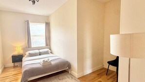 Un dormitorio con cama, mesita de noche, lámpara y vistas de la ciudad a través de una ventana.