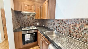 Una cocina compacta con armarios de madera, protector contra salpicaduras de cerámica, un lavamanos de acero inoxidable y un lavavajillas.