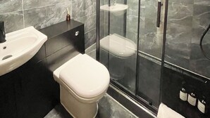 Un baño moderno con ducha envuelta en vidrio, un inodoro blanco, un lavamanos negro y un espejo.
