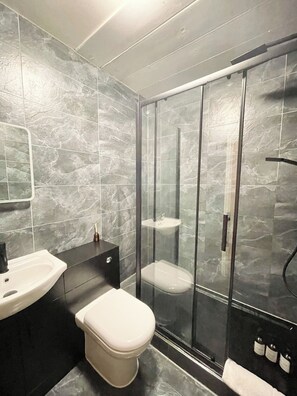 A modern bathroom with a glass-enclosed shower, a white toilet, a black sink, and a mirror. - Spacious One-Bedroom Gem in Central Earls Court (Greater London)