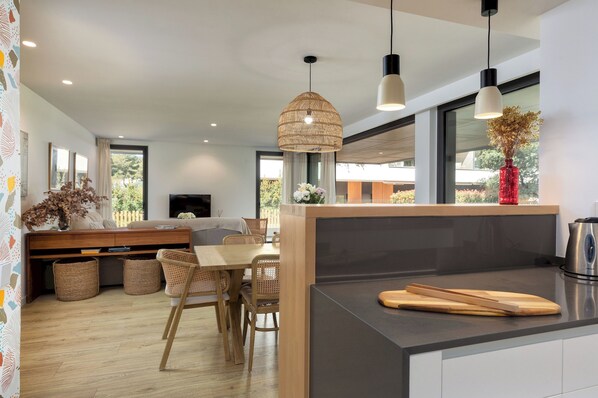A modern kitchen with a central island, dining area with wicker chairs, and large windows. - Solina | Swimming Pool | Terrace | Palamos (Palamos)