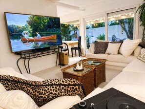 Ein Wohnzimmer mit Fernseher, Sofa, Couchtisch und Blick auf einen Garten.