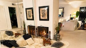 Un salon chaleureux avec une cheminée, des fauteuils confortables et des œuvres d’art encadrées accrochées aux murs.