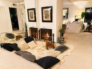 Ein gemütliches Wohnzimmer mit Kamin, bequemen Sitzmöglichkeiten und gerahmten Kunstwerken an den Wänden.