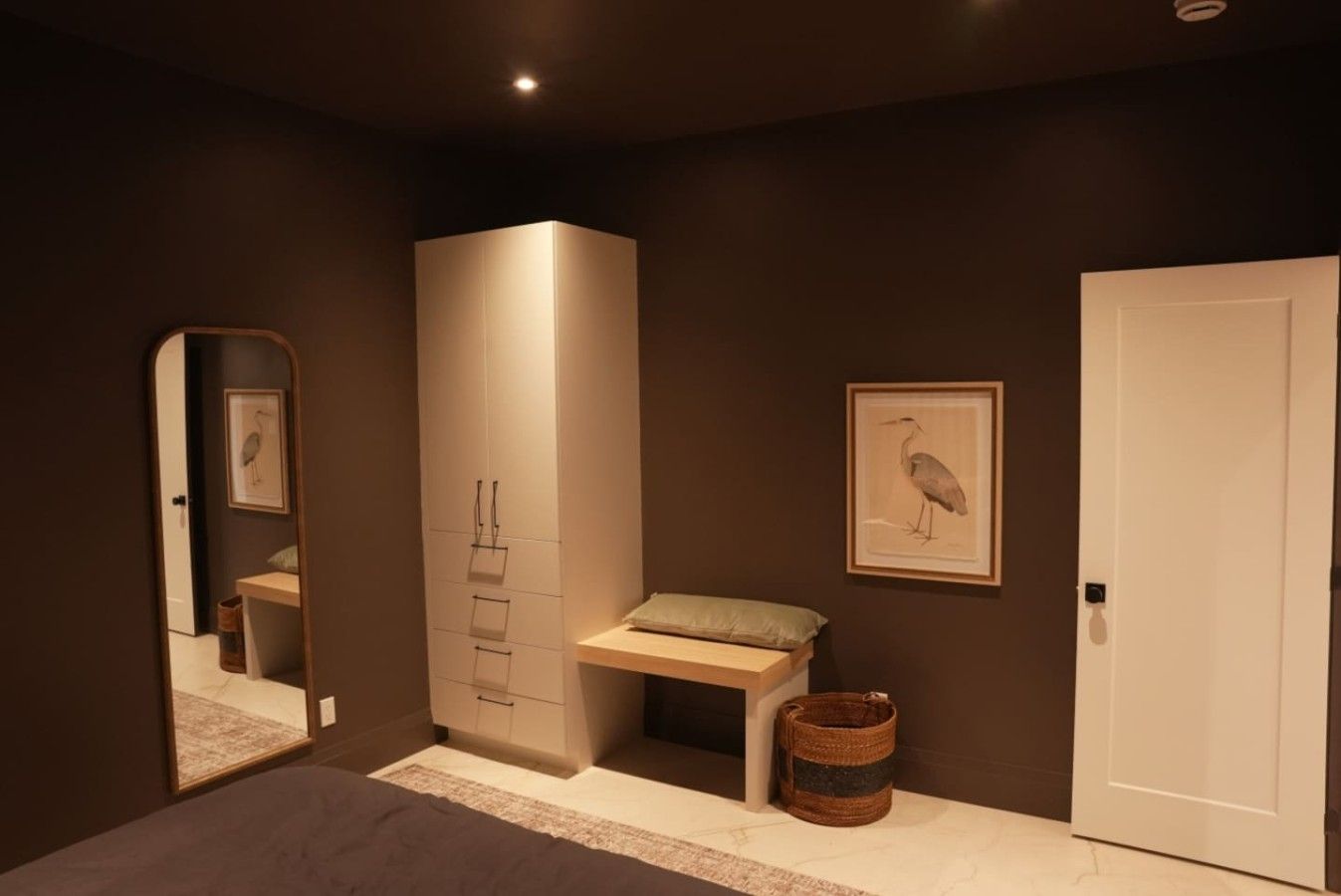 A bedroom with a bed, a wardrobe, a bench, a framed picture, a door, and a mirror.