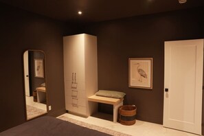Une chambre à coucher comprenant un lit, une armoire, un banc, un tableau encadré, une porte et un miroir.