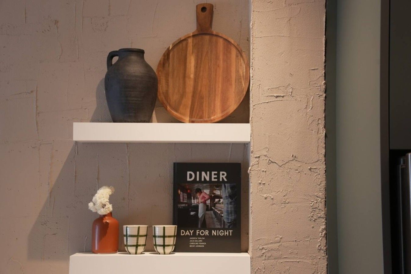 A shelf with a book titled 'DINER' and a wooden cutting board.