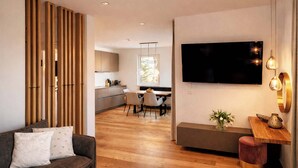A modern living room with a sofa, a dining area with chairs, a TV mounted on the wall, and a wooden partition. - ZILLER DELIGHT – Stylish Apartment with Balcony & Mountain View (Fügen)