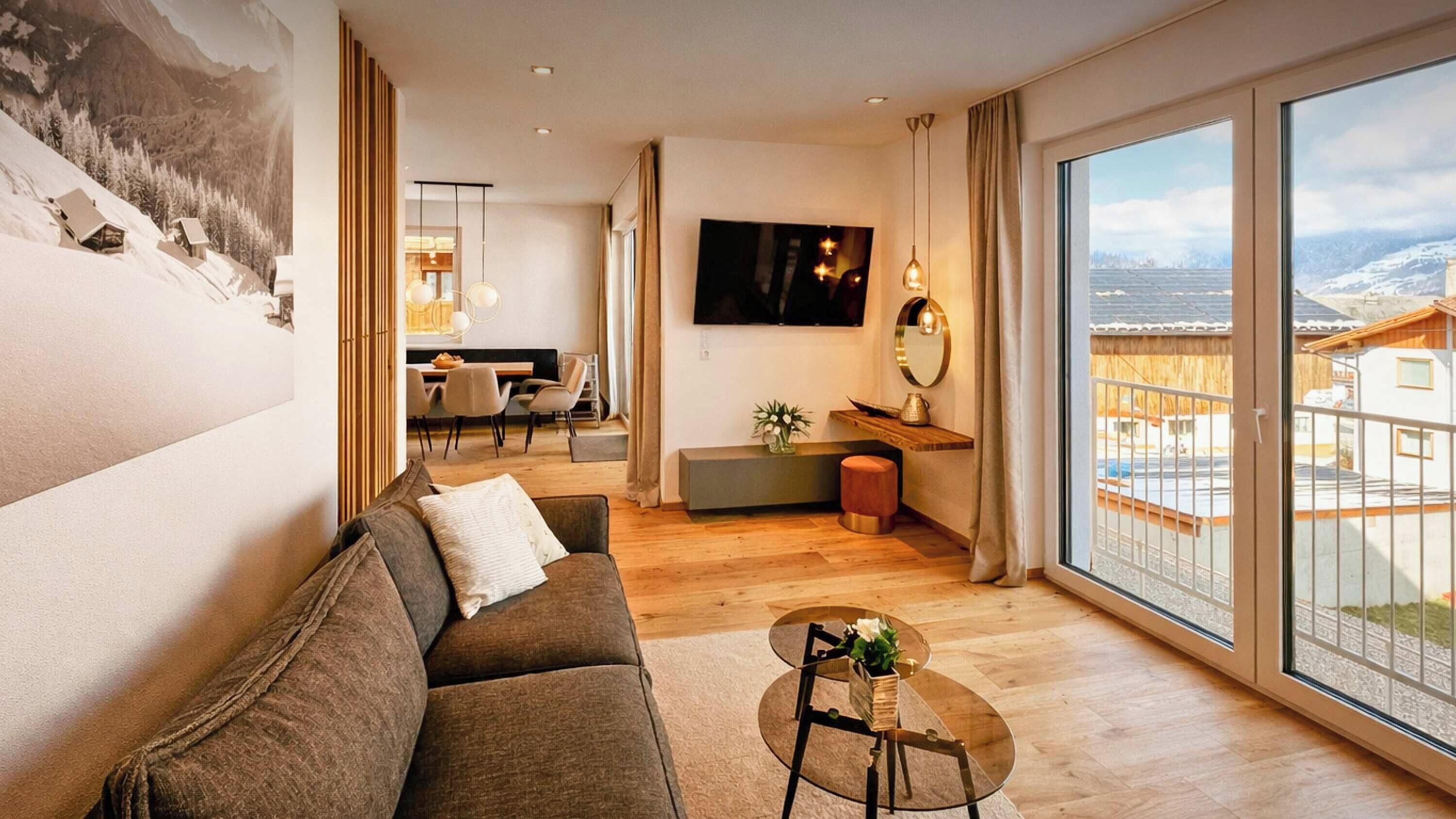 Een moderne woonkamer met een groot raam, een bank, een salontafel en een aan de muur bevestigde televisie.