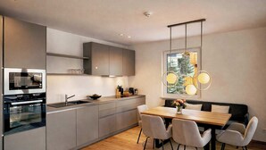 A modern kitchen with built-in appliances, a dining area with a wooden table and chairs, and a large window with a view. - ZILLER DELIGHT – Stylish Apartment with Balcony & Mountain View (Fügen)