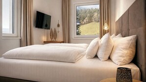 A bedroom with a bed, a TV, a window with a view of a hill, and a lamp. - ZILLER DELIGHT – Stylish Apartment with Balcony & Mountain View (Fügen)