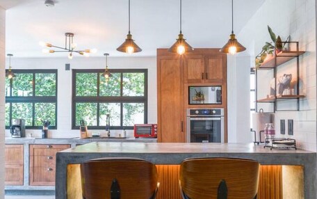A modern kitchen with wooden cabinets, a central island with bar stools, pendant lighting, and a view of the outdoors.