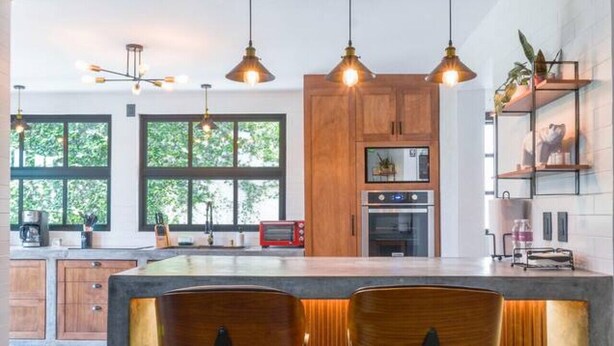 A modern kitchen with wooden cabinets, a central island with bar stools, pendant lighting, and a view of the outdoors.