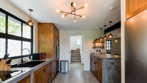 A modern kitchen with wooden cabinets, a stainless steel refrigerator, and pendant lighting.