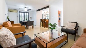 A modern living room with a glass coffee table, leather sofas, a dining area with a table and chairs, and a kitchen in the background.