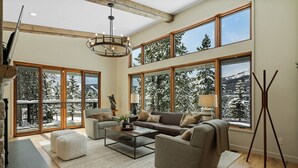 A spacious living room with a large sofa, two armchairs, a coffee table, and a fireplace. Large windows offer a view of snow-covered trees. - *New Listing* Swift Bear Ski-In/Out Lodge (Big Sky)