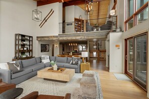 Ein großzügiger Wohnbereich mit einer großen Couch, einem Couchtisch und einem Kamin. Eine Treppe führt zu einer oberen Ebene mit einem Balkon.