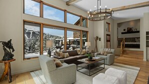 A spacious living room with large windows, a fireplace, and a staircase leading to an upper level. - *New Listing* Swift Bear Ski-In/Out Lodge (Big Sky)