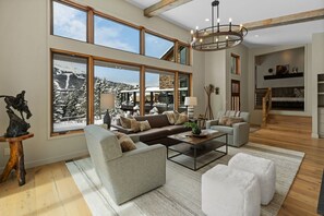 Ein geräumiges Wohnzimmer mit großen Fenstern, einem Kamin und einer Treppe, die in eine obere Etage führt.