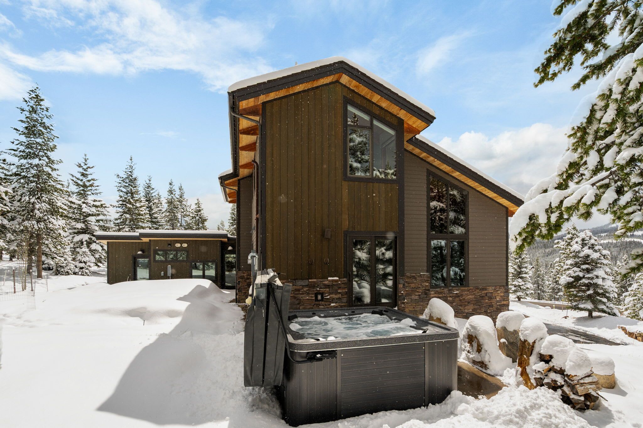 A modern wooden cabin with a hot tub in the snow.