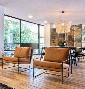 A modern interior with two leather armchairs, a dining table, and a large window offering a view of greenery. - Beautiful Curated and Designed Flat plus Great Balcony (Mexico City)
