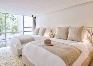 Ein modernes Schlafzimmer mit zwei Betten, einem großen Fenster und Blick auf Grünflächen.