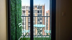 Ein Balkon mit Blick auf ein Gebäude, eine grüne Wand und ein Tisch mit Stühlen.