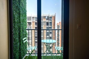Un balcón con vistas a un edificio, un muro verde y una mesa con sillas.