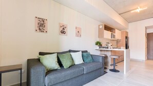 Ein modernes Wohnzimmer mit einem grauen Sofa, einem kleinen Beistelltisch und einer Küchenzeile mit einer Bar.