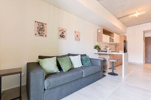 Una sala de estar moderna con un sofá gris, una mesita auxiliar y una zona de cocina con barra.