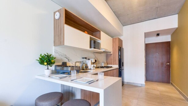 Eine moderne Küche mit Marmorarbeitsplatte, Holzschränken und einem eingebauten Ofen. Auf der Arbeitsplatte stehen zwei Hocker und ein Blumentopf.