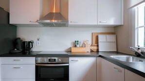 Una cocina moderna con armarios blancos, una campana extractora de acero inoxidable, un horno empotrado, una cafetera y una tabla de cortar de madera.