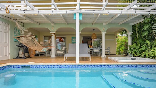 Una piscina con un pérgola blanca, una hamaca y una zona de comedor con sillas y mesas.
