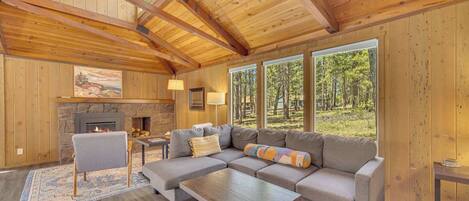 A cozy living room with a fireplace, large windows, and a wooden ceiling.