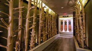A corridor with a unique wooden wall design, a tiled floor, and a door with a red exit sign.