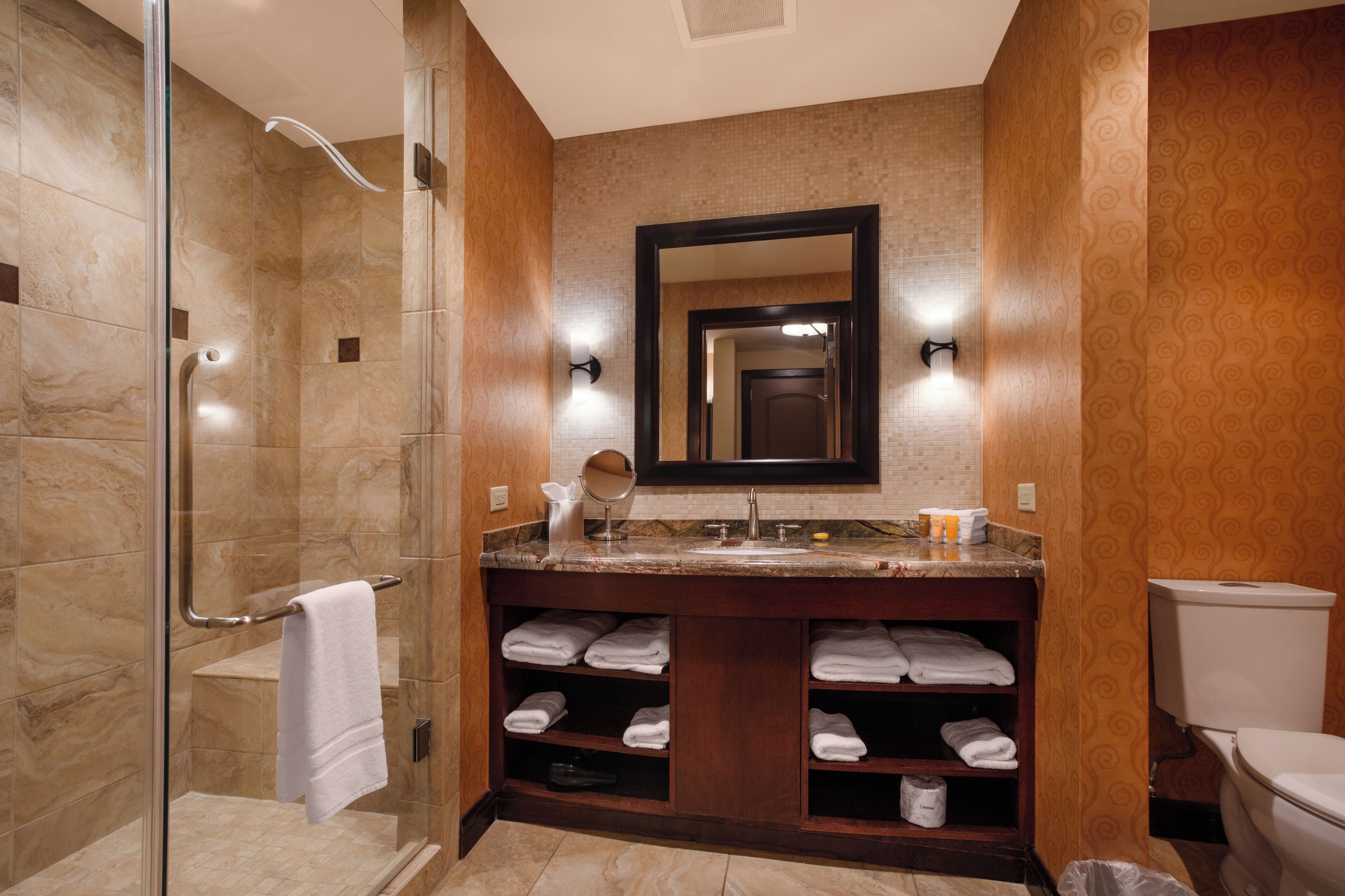 Un baño con cabina de ducha de vidrio, tocador con espejo y retrete.