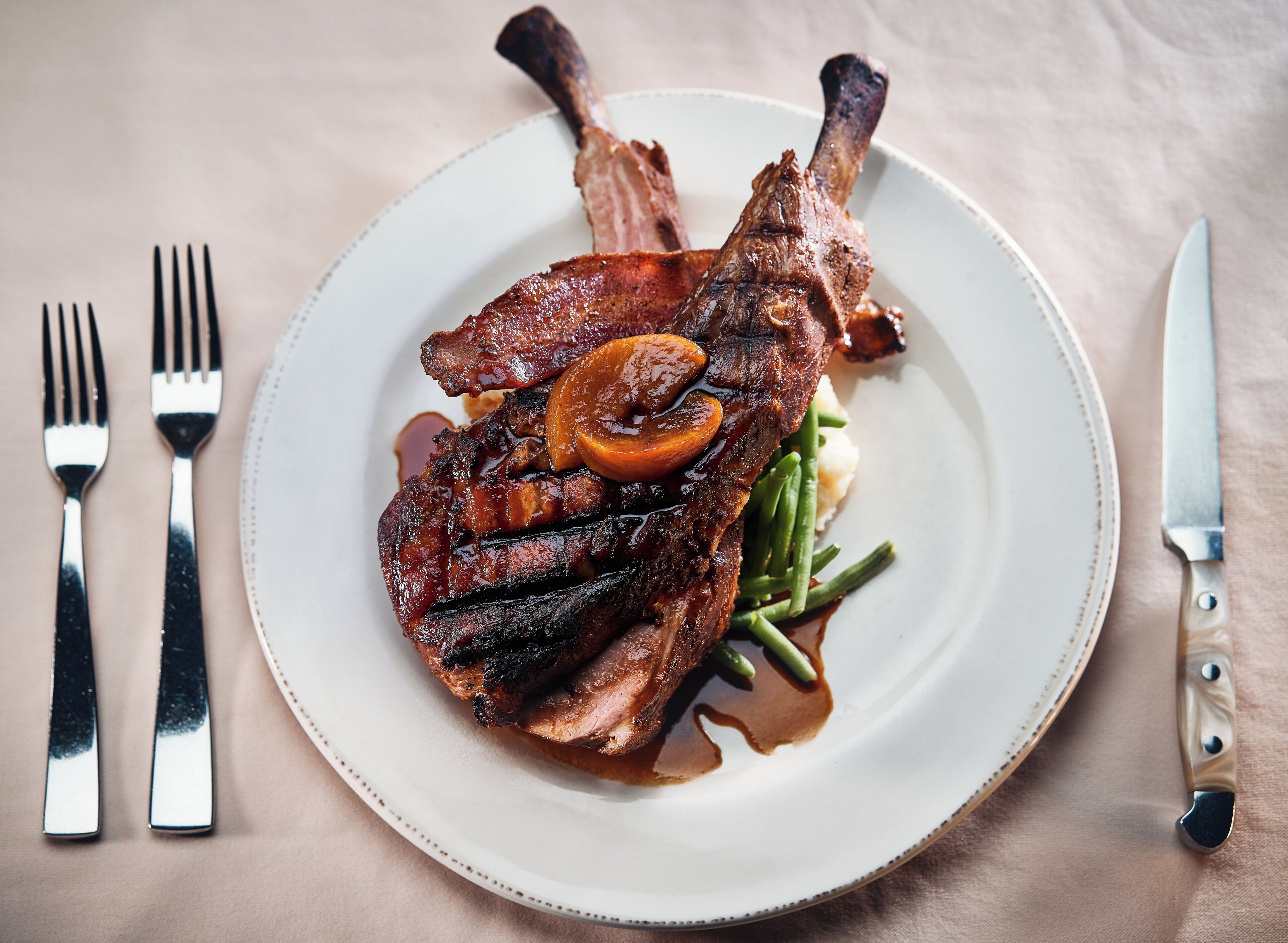 A plate with a lamb shank, green beans, and a slice of carrot.