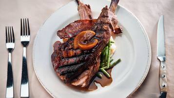 A plate with a lamb shank, green beans, and a slice of carrot.