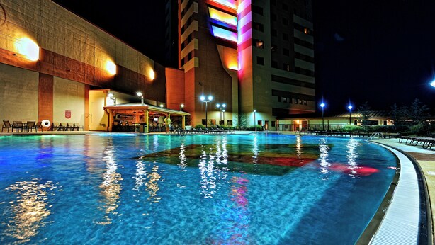 Una piscina con reflejos de luces, un edificio de fachada singular y una zona de bar.
