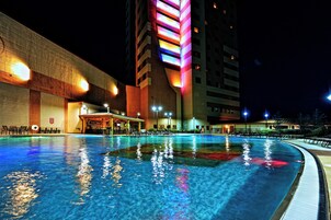 Una piscina con reflejos de luces, un edificio de fachada singular y una zona de bar.