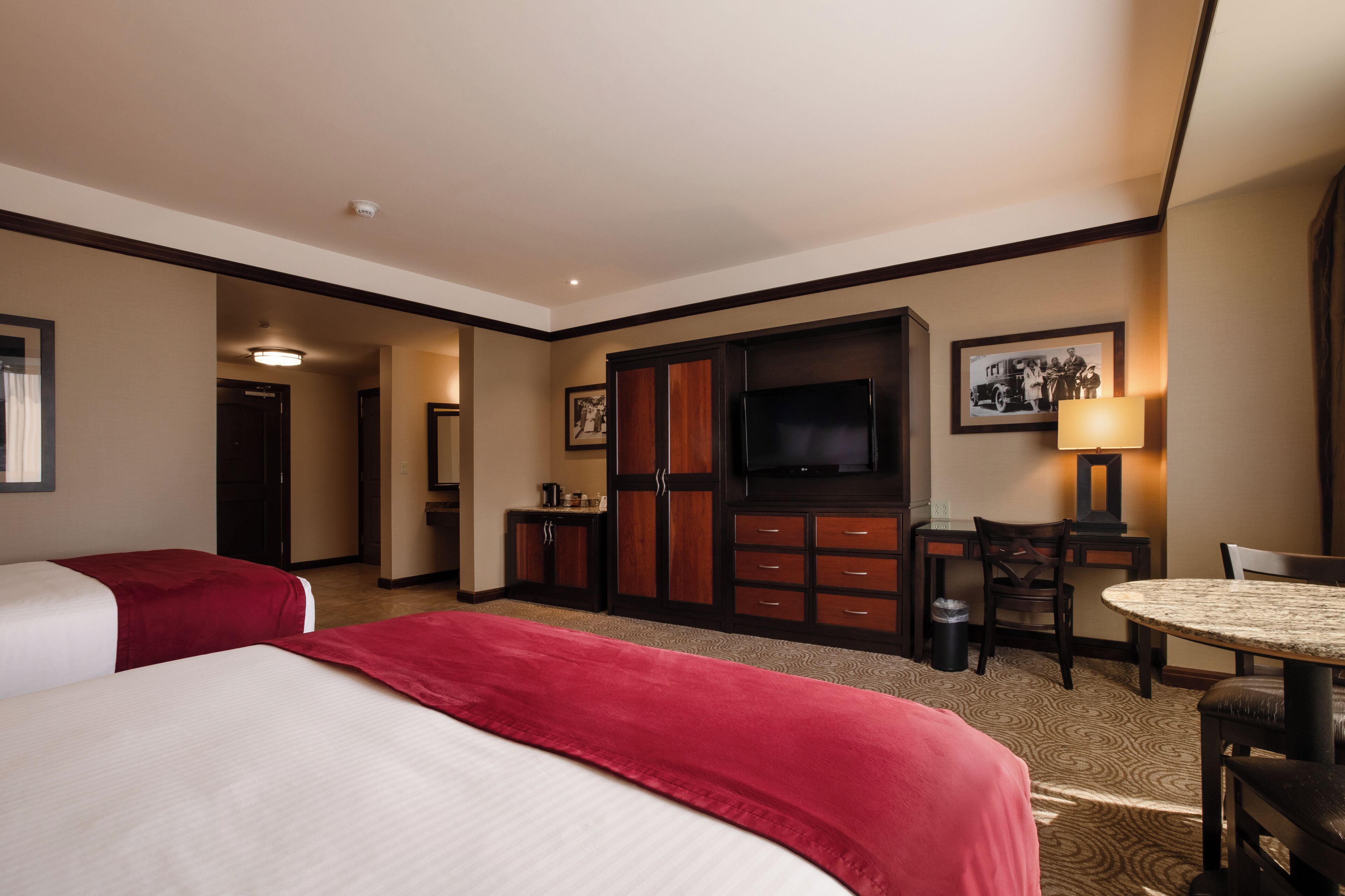 Ein Hotelzimmer mit zwei Betten, einem Fernseher, einem Schreibtisch mit Stuhl und einem kleinen Tisch.