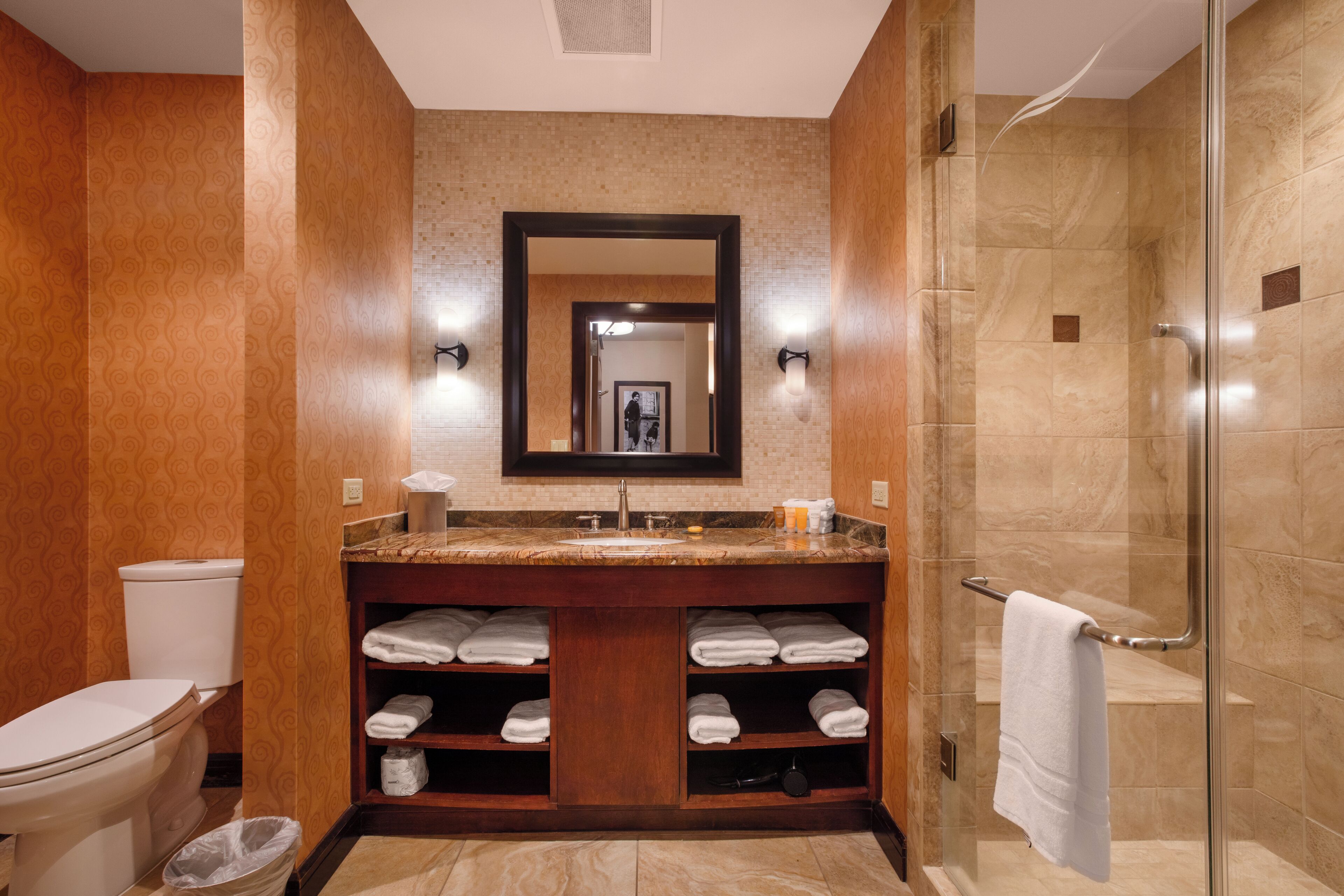 A bathroom with a toilet, sink, mirror, shower, and towel storage.