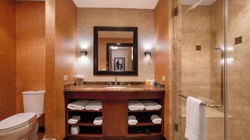 A bathroom with a toilet, sink, mirror, shower, and towel storage.