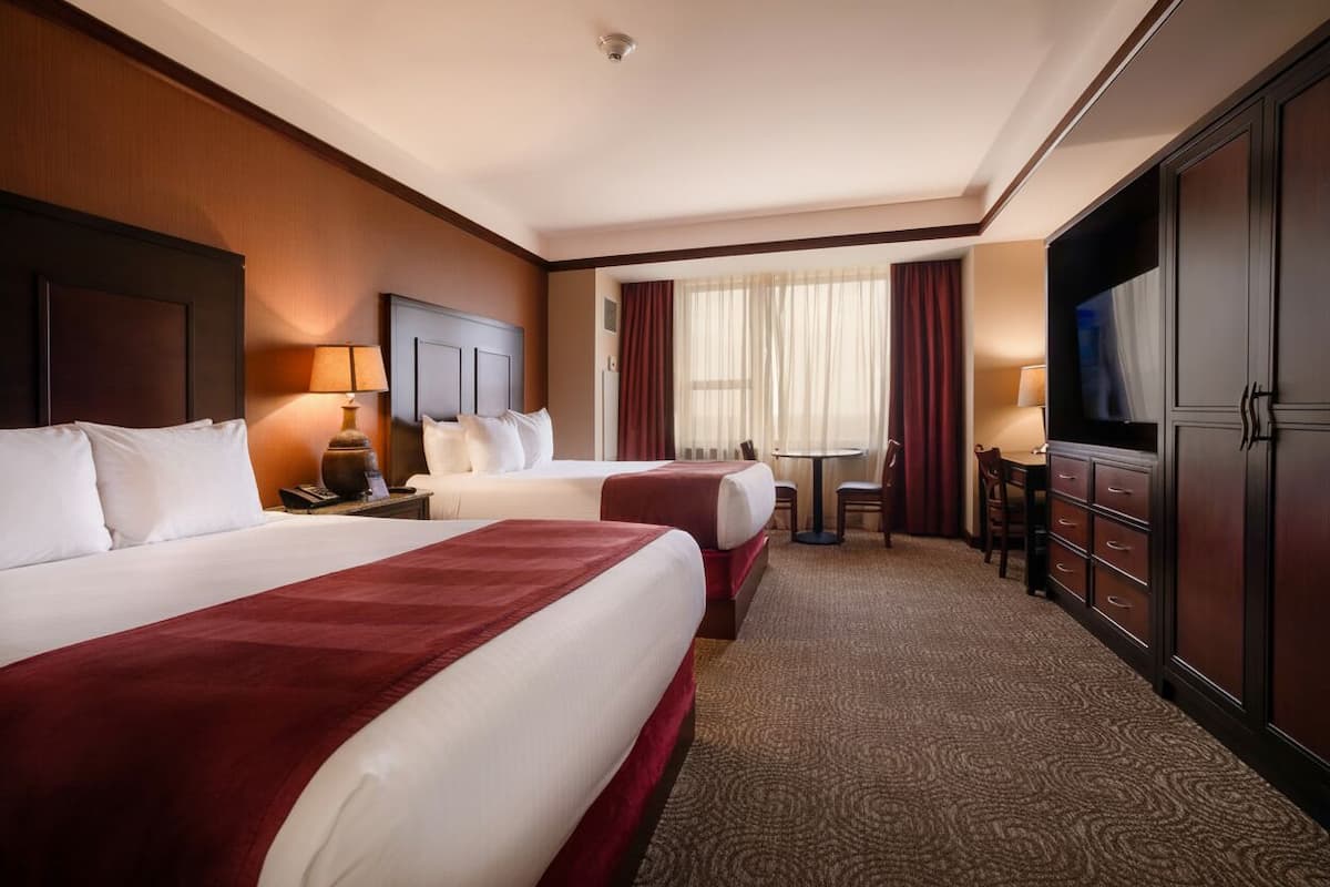 Habitación de hotel con dos camas, un escritorio, una silla, un televisor y un armario.