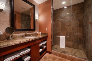 A bathroom with a marble countertop, a large mirror, a glass-enclosed shower, and a towel rack. - Downstream Casino Resort (Quapaw)
