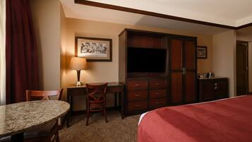 Habitación de hotel con cama, escritorio, sillas, televisor y armario.