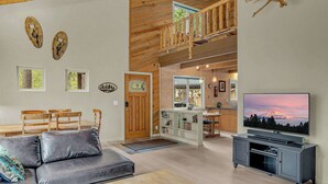 Uma sala de estar ampla com teto de madeira, um sofá, uma mesa de centro e uma televisão.
