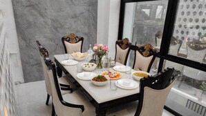 A dining table set with plates, bowls, and glasses, surrounded by chairs with ornate backs. - Enjoy your staycation in lonavala with our luxurious villa. (Lonavala)