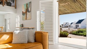 A modern living room with a sofa, a painting, and a view of a residential area. - Waterbird Coastal Retreat (Velddrif)